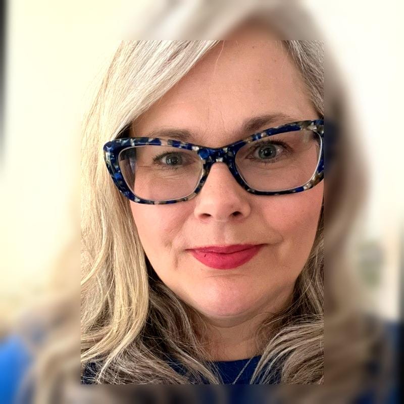 headshot of Pernille perry. Long grey hair, glasses and a blue top
